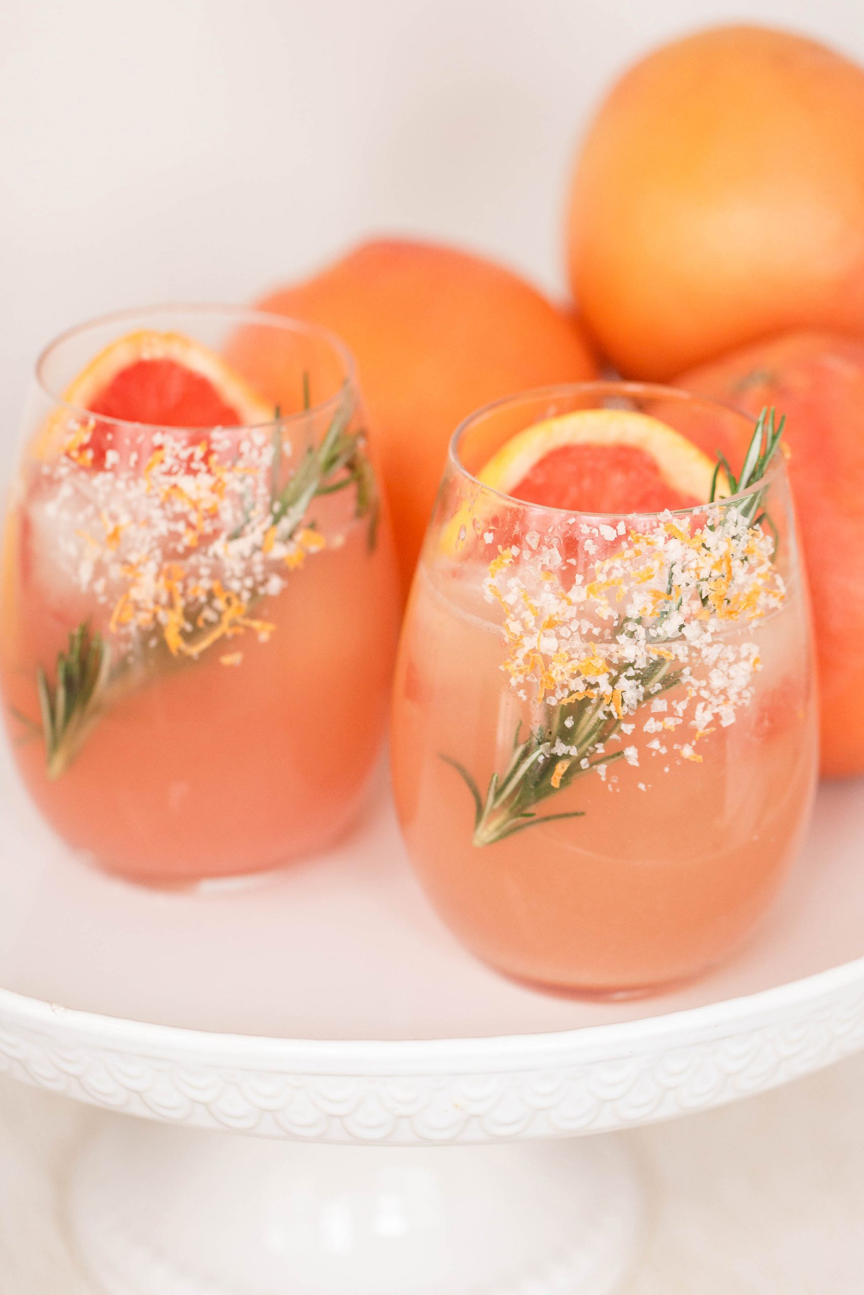 addison: A Paloma cocktail with large clear ice cubes in a tall collins  glass garnished with a grapefruit peel on a white marble counter top