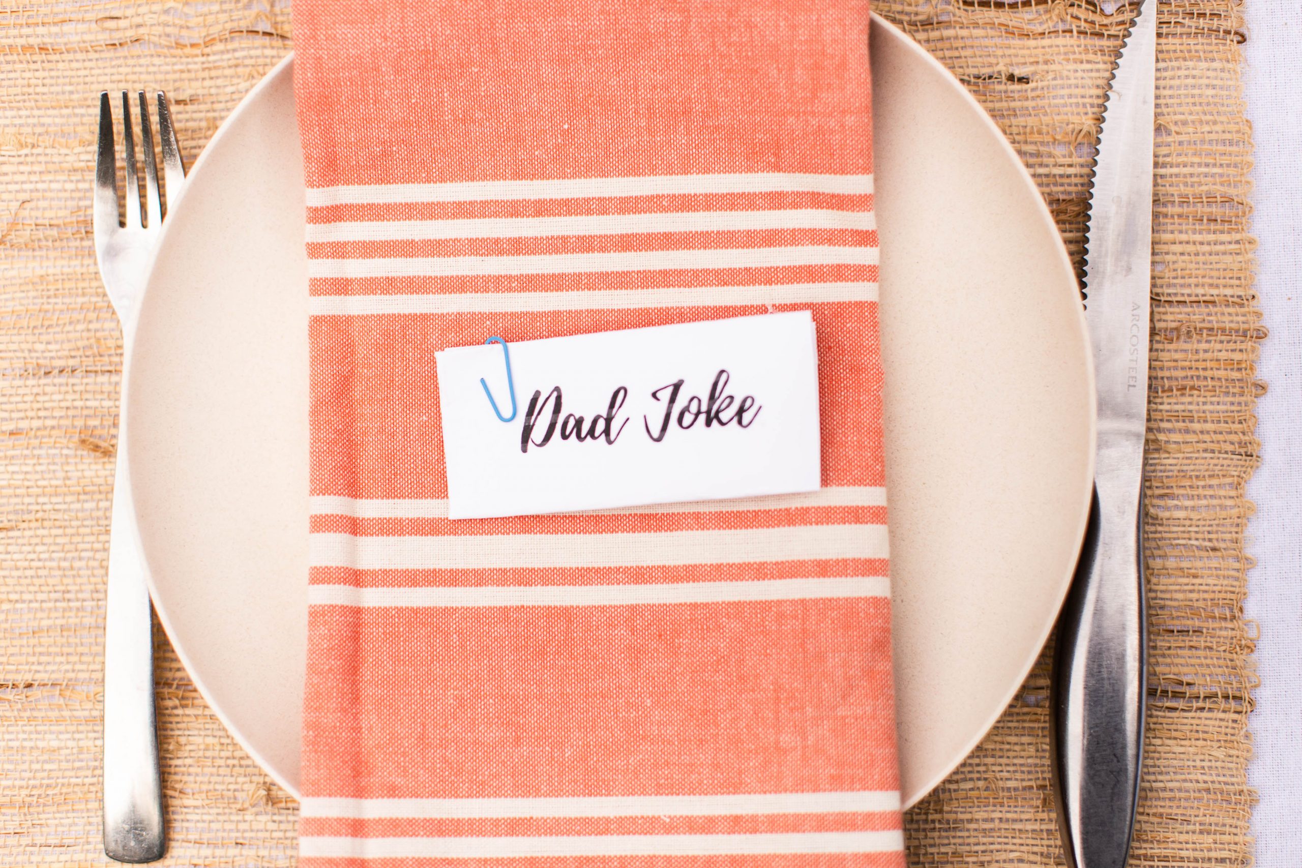 table setting for Father's Day. Bamboo plate, Dad Joke on piece of paper, coral striped dinner napkin