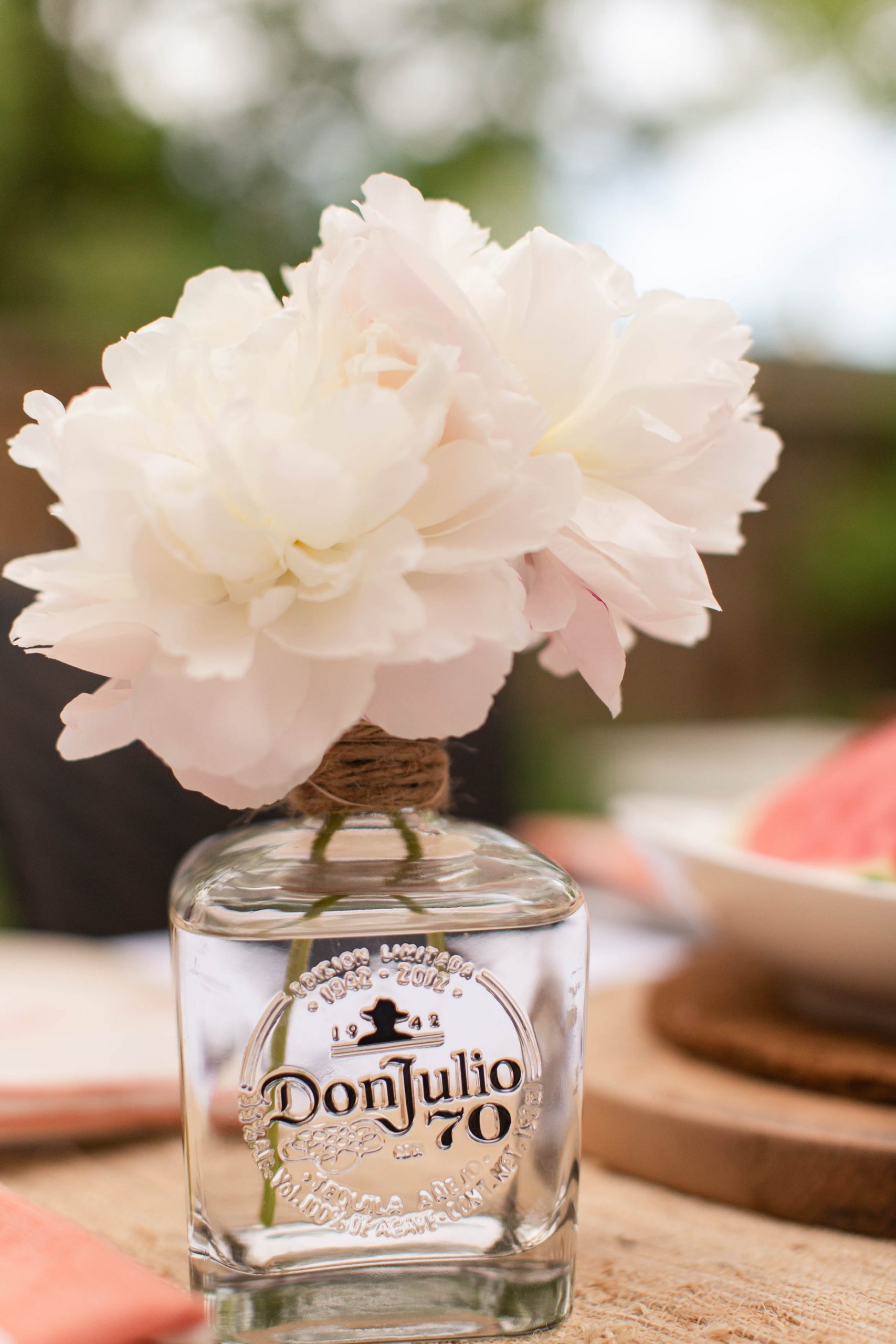 white peonies in old tequila bottle vase